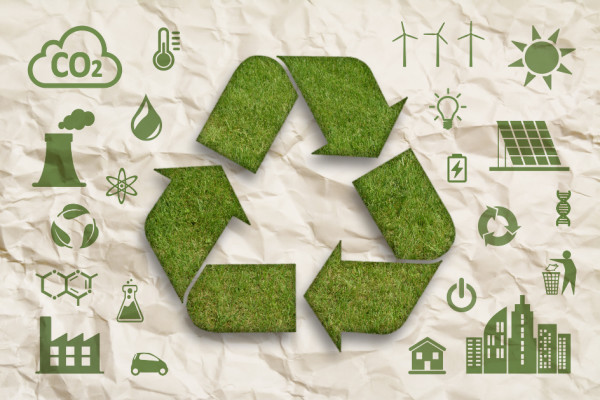 Símbolo de reciclagem em grama sobre papel amassado com ícones de sustentabilidade ao redor.