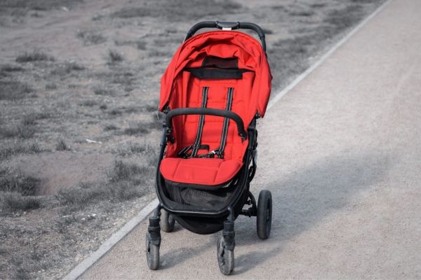 Carrinho de bebê vermelho vazio em uma estrada de terra.