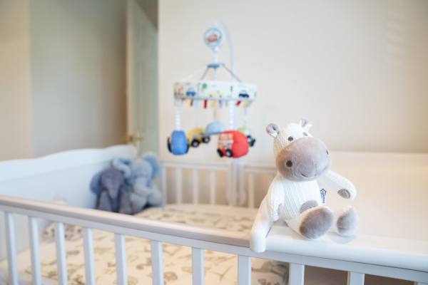 A tidy nursery with a plush toy on a white crib and a mobile hanging above.