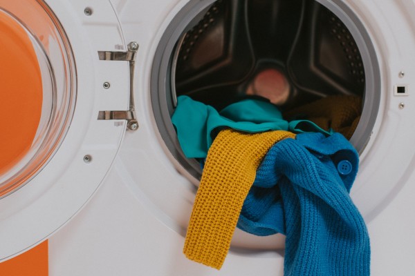 Open washing machine door with colourful clothing partially inside.