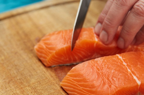 A person slicing raw salmon on a wooden chopping board.