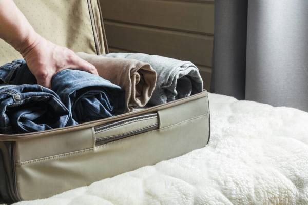 A person packing neatly rolled clothing into a suitcase.