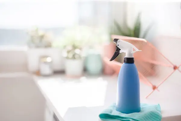 A spray bottle on a microfiber cloth with blurred plants and decor in the background.
