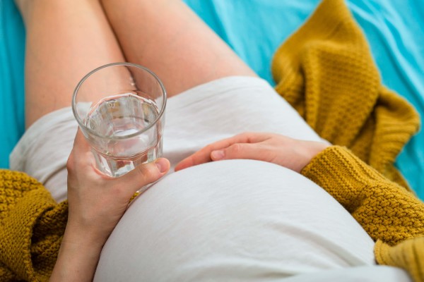 Pregnant person relaxing with a glass of water.