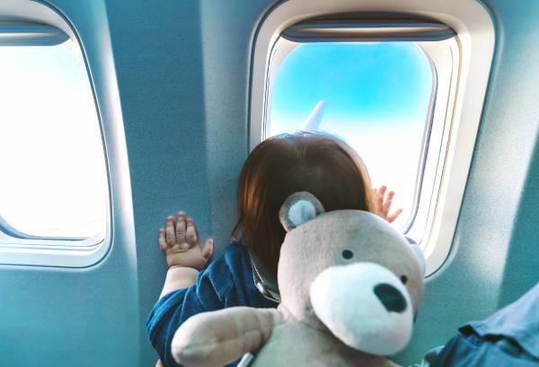 Child with teddy bear looking out of an airplane window.