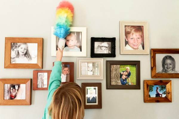 A child dusting a wall of framed photographs with a colourful feather duster.