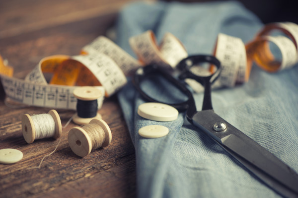 Sewing materials including scissors, thread spools, measuring tape, and buttons on a piece of denim fabric.