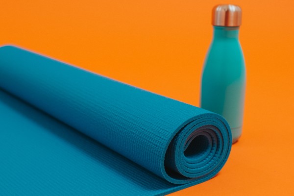 A rolled-up blue yoga mat and a blue water bottle on an orange background.
