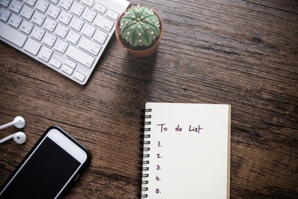 A tidy workspace with a keyboard, a small potted cactus, a notebook with 'To do List' written on it, a smartphone, and earphones on a wooden surface.