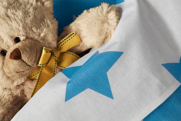 A teddy bear with a yellow bow lying on a blue and white star-patterned fabric.