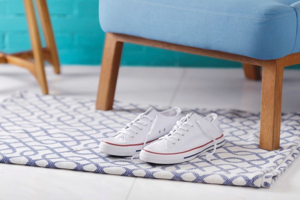 A pair of white sneakers on a patterned rug under a blue ottoman with wooden legs.