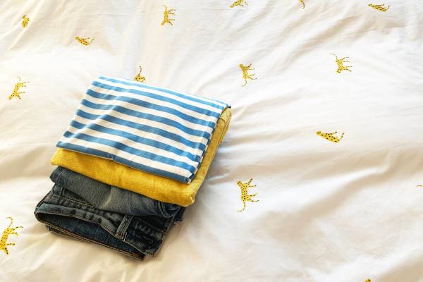 A neatly folded pile of clothes on a bed with a banana-patterned duvet cover.