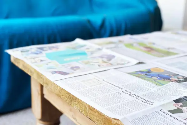 An open newspaper on a wooden coffee table with a blurry blue sofa in the background.