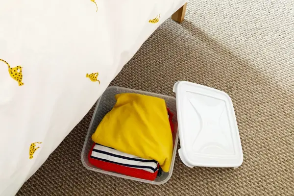 Under-bed storage container with clothes next to a bed with patterned sheets.