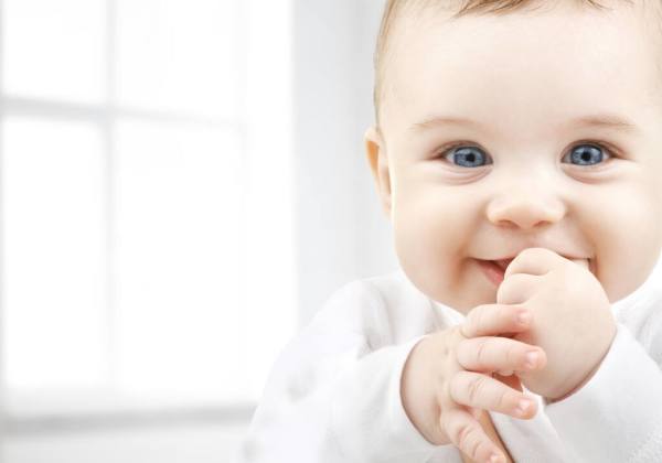 A smiling baby with blue eyes wearing a white outfit.