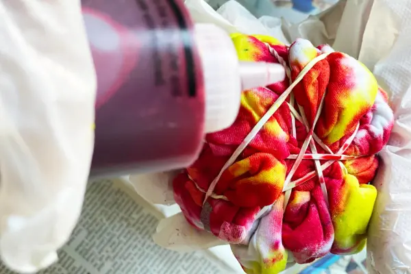 A fabric being tie-dyed with bright red and yellow dyes.