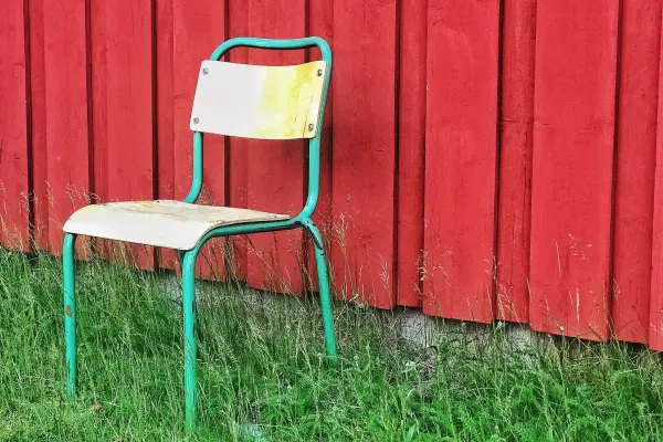 A weathered metal chair against a red wooden wall.