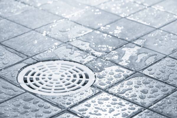 Wet tiled floor with a central drain and water droplets.
