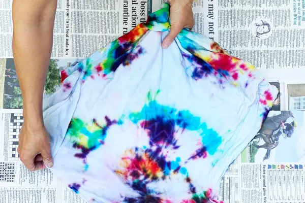 Person holding a tie-dye shirt over a newspaper-covered table.