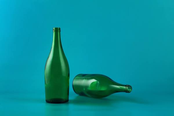 Two empty green glass bottles against a blue background, one standing upright and the other lying down.