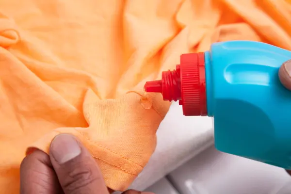 Blue detergent bottle being used on an orange fabric.