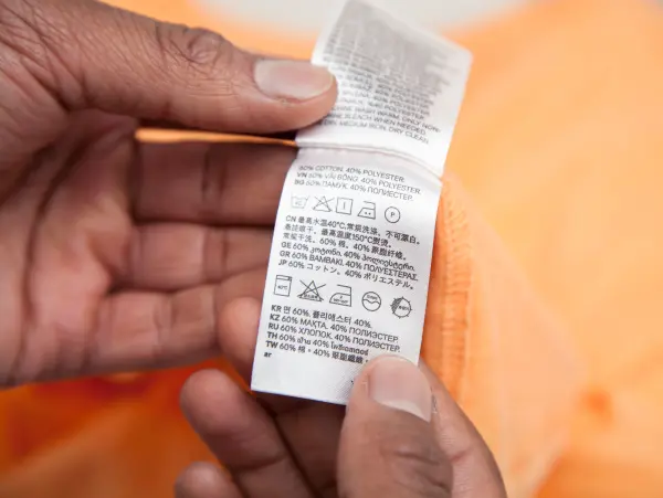 A close-up of a person's hands holding a clothing care label showing fabric content and washing instructions.