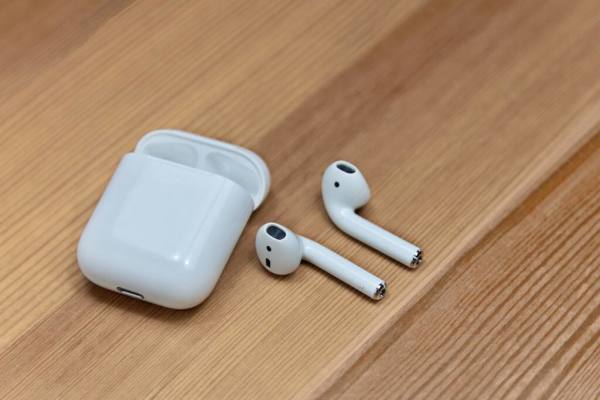 White wireless earbuds with open charging case on a wooden surface.