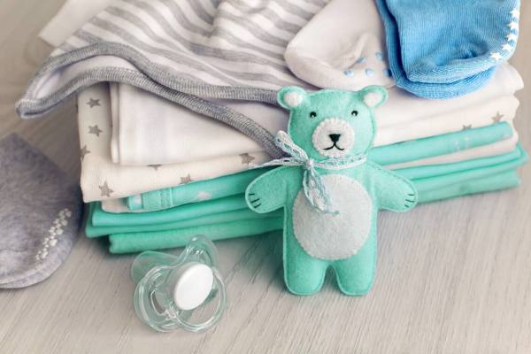 Neatly stacked baby clothes with a felt teddy bear and a pacifier.