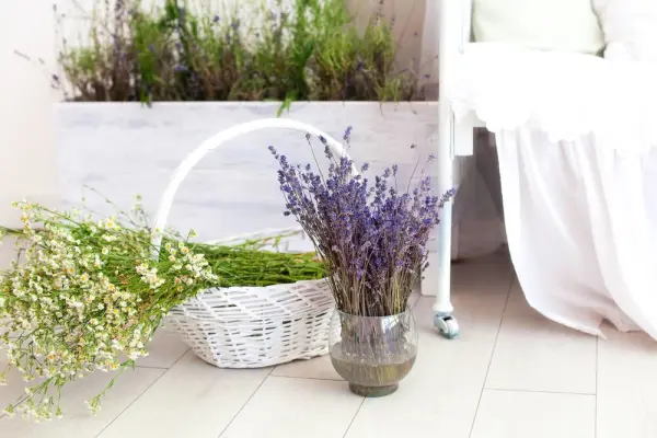 Karangan bunga lavender dalam vas kaca dan keranjang putih dengan bunga di lantai kayu.