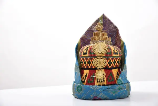 Topi adat Indonesia berwarna-warni dengan hiasan emas di atas latar belakang putih.