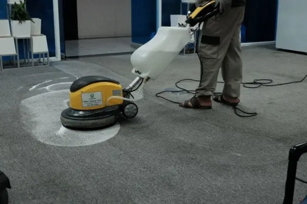 Người lau sàn bằng máy chà sàn điện trong một không gian văn phòng.