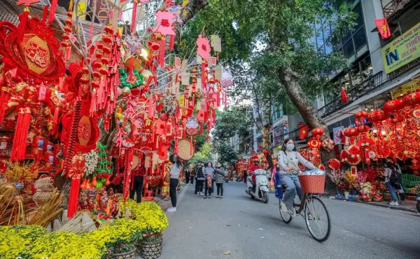 Phố bán hàng trang trí Tết với nhiều đèn lồng và hoa mai, người đi xe đạp và người đi bộ.