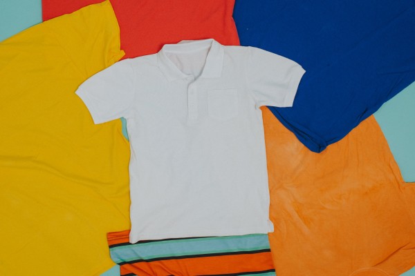 Áo polo trắng và quần shorts nhiều màu xếp gọn trên nền màu xanh pastel.