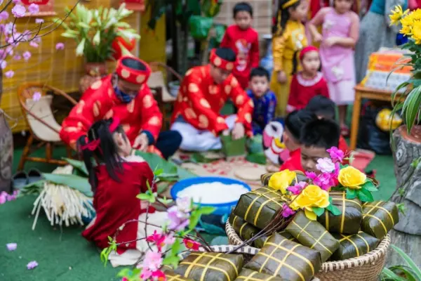 Người lớn và trẻ em mặc trang phục truyền thống màu đỏ, đang chuẩn bị bánh chưng và thưởng thức không khí Tết Nguyên Đán.
