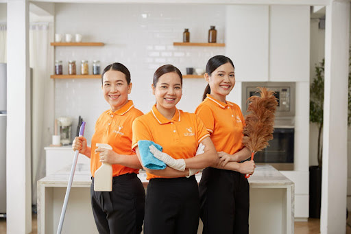 Ba người phụ nữ mặc đồng phục màu cam với dụng cụ làm sạch trong căn bếp.