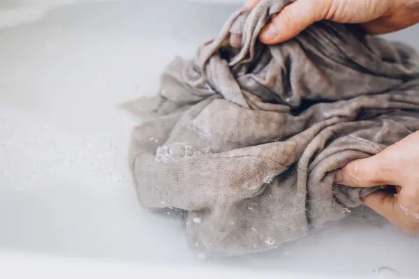 Một người đang giặt quần áo bằng tay trong bồn nước xà phòng.