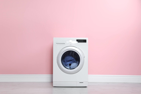 Eine Waschmaschine mit Wäsche darin, vor einer rosa Wand und auf einem Holzboden.