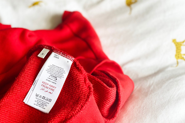 Prenda roja con etiqueta de cuidado sobre tela blanca con manchas.
