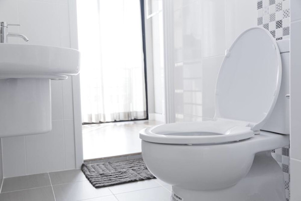 Kamar mandi yang bersih dan terang dengan toilet putih dan wastafel.