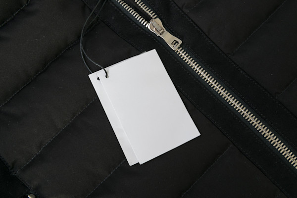 A blank white label attached to a black garment with a zipper.