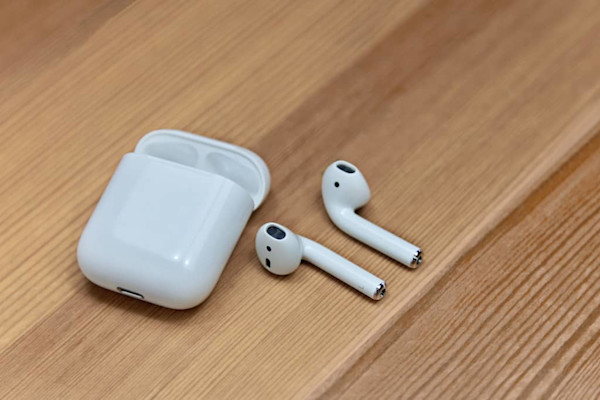 Earphone nirkabel putih dan kotak pengisiannya di atas meja kayu.
