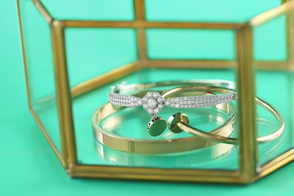 A diamond ring and a plain band inside a gold-rimmed glass box with a turquoise background.