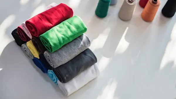 Baju yang dilipat rapi dan beberapa benang jahit di atas meja.