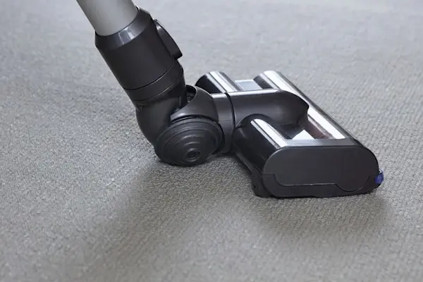 A vacuum cleaner nozzle on a gray carpet.