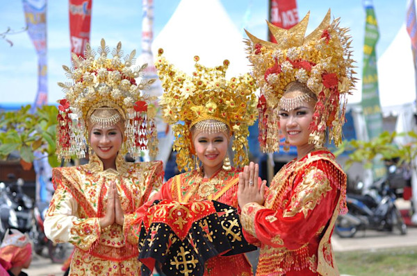 Tiga penari wanita dengan kostum adat Minangkabau berhias emas dan merah menyapa dengan tangan terlipat.