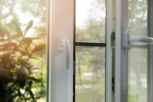 Sunlit open window with a view of greenery outside, including a focus on window handles.