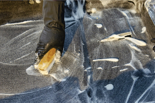 A person scrubbing a carpet with a brush and soapy water.