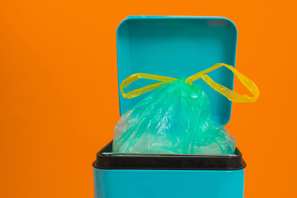 Tempat sampah biru dengan kantong sampah hijau yang terikat di atas latar belakang oranye.