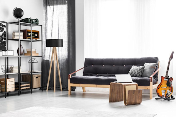 Ein modernes Wohnzimmer mit einem schwarzen Sofa, Metallregalen, Stehlampe, Gitarre und einem Laptop auf einem Couchtisch.