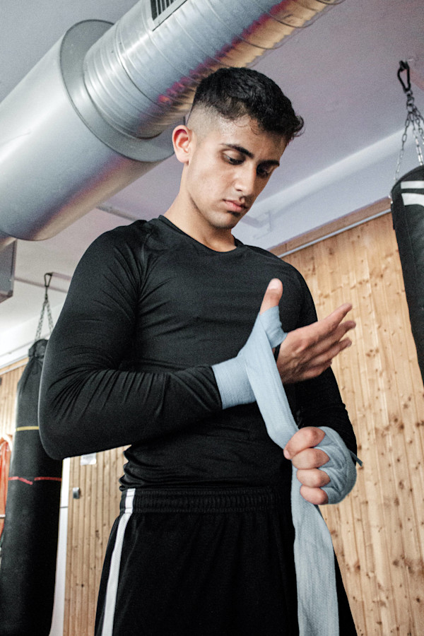 Junger Mann wickelt eine Boxbandage um seine Hand in einem Fitnessstudio.